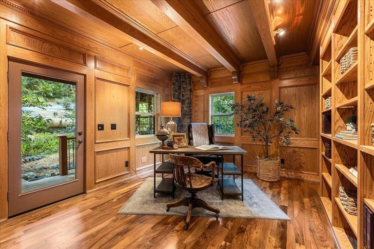 Cozy home office includes built-in bookshelves, a wood desk, and an outdoor view through a glass door. coldwellbanker-nevada-city-ca-jan0925-8