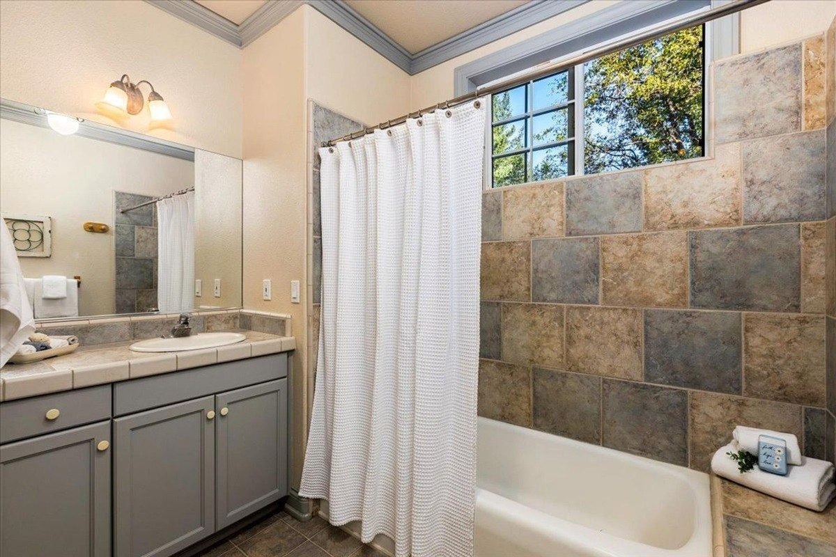 Bathroom showcases a tile-surround bathtub, grey vanity, and a large mirror beneath bright lighting.