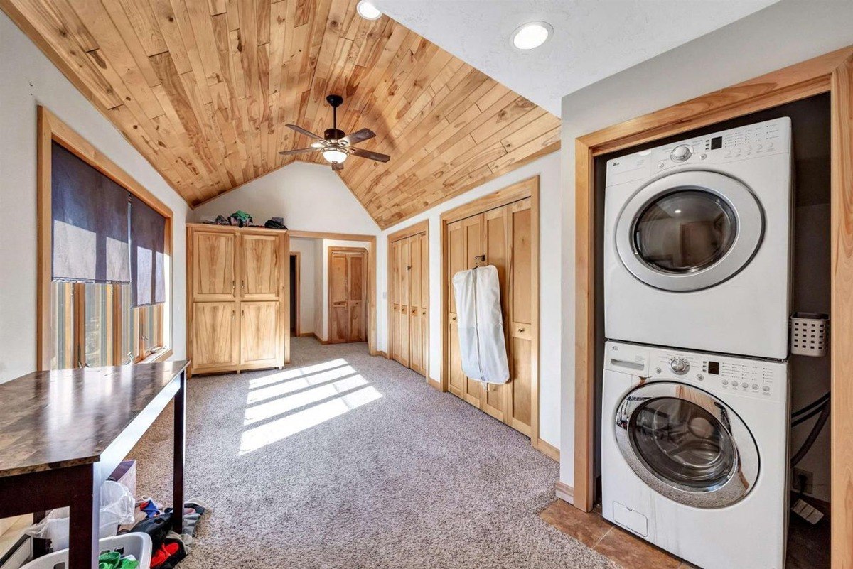 Laundry room featuring a stacked washer and dryer, wood storage cabinets, and a vaulted ceiling with natural wood paneling.