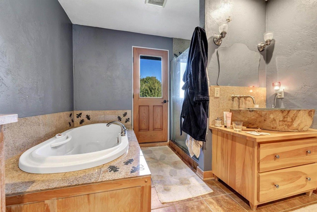 Bathroom with a corner bathtub, natural stone accents, and a vanity featuring a vessel sink and wooden cabinetry.