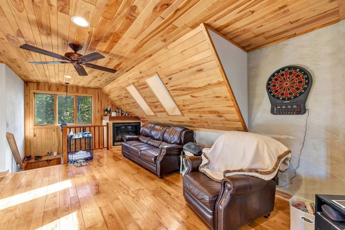 Loft-style living area with sloped wooden ceilings, leather seating, a fireplace, and a dartboard on the wall.