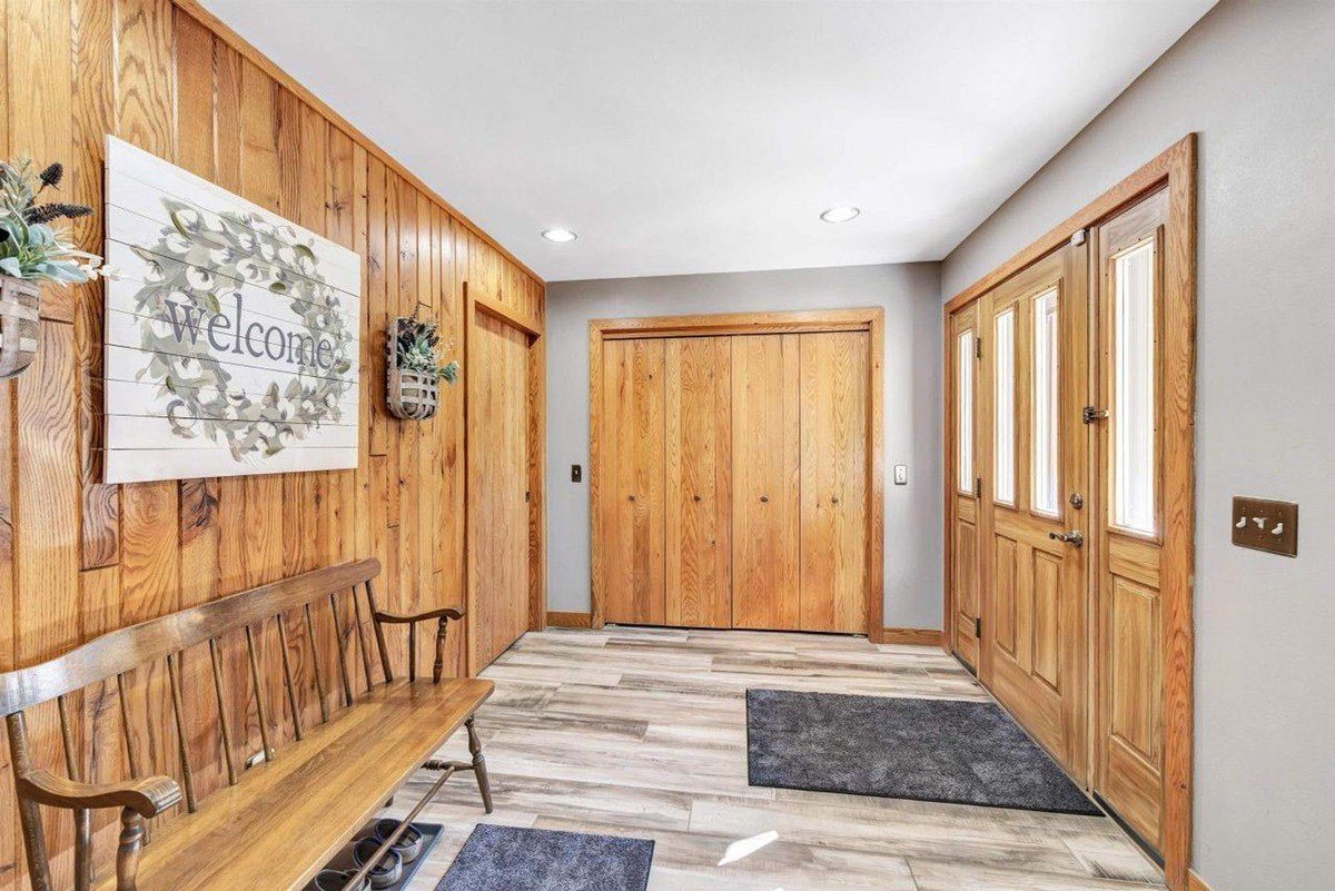 Entryway has wood walls, floors, and doors, with a bench and welcome sign.