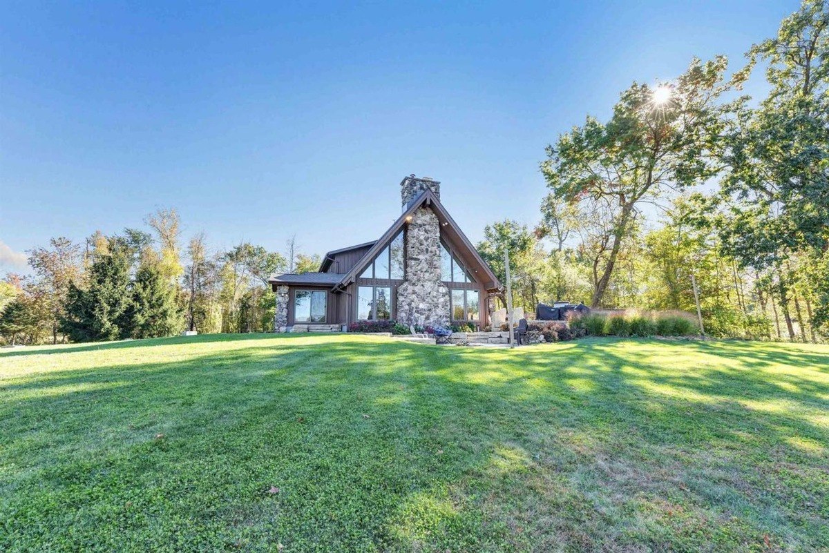 Modern house with a large stone chimney surrounded by greenery and trees under clear blue skies.