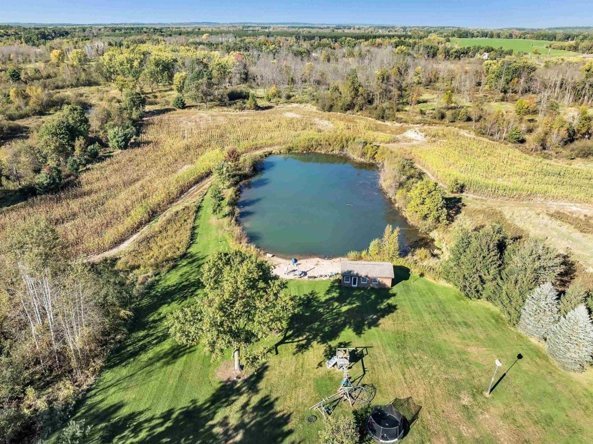 Aerial view of a serene property featuring a pond, green fields, and a playground setup near the shore.