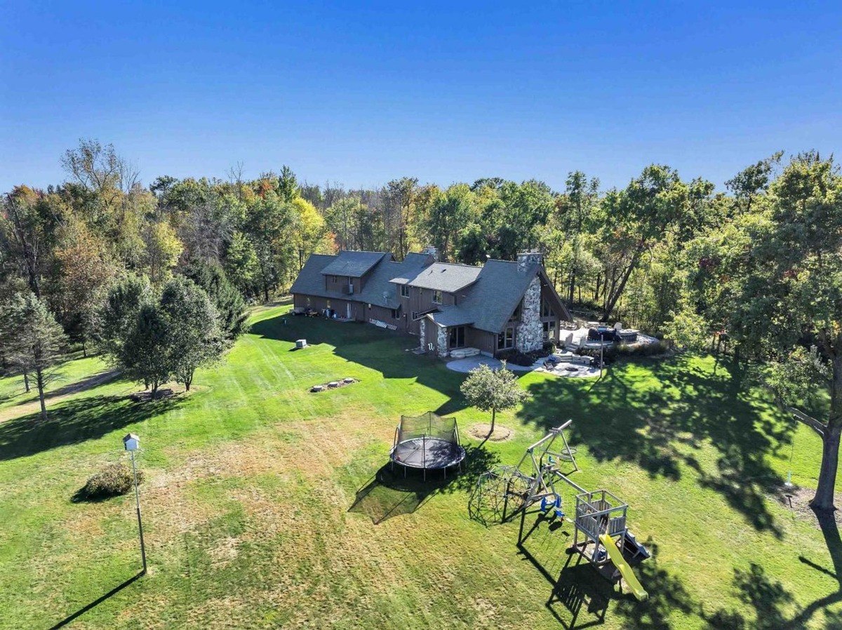 Rear exterior displays a wide backyard with a playground and the house's large, rustic design.