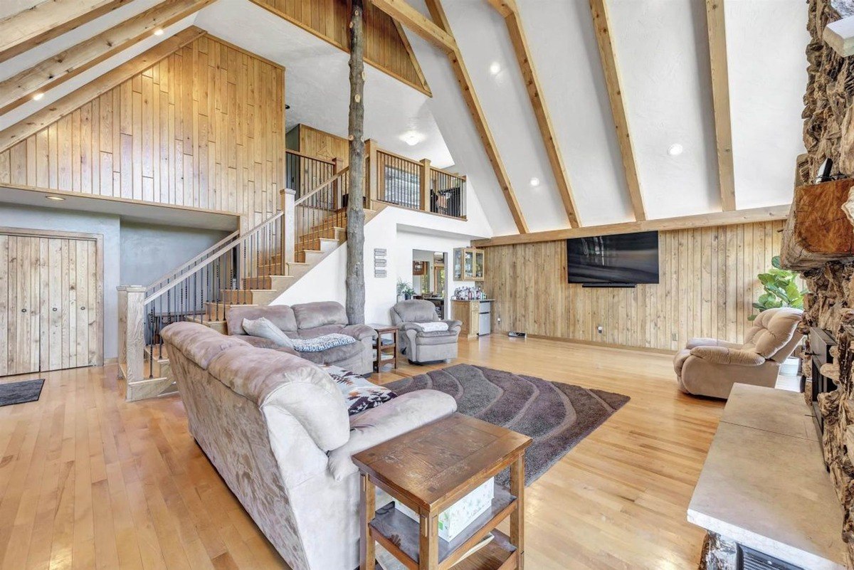 Living room with vaulted ceilings, wood walls and floors, large sectional sofa, and a flat-screen TV.