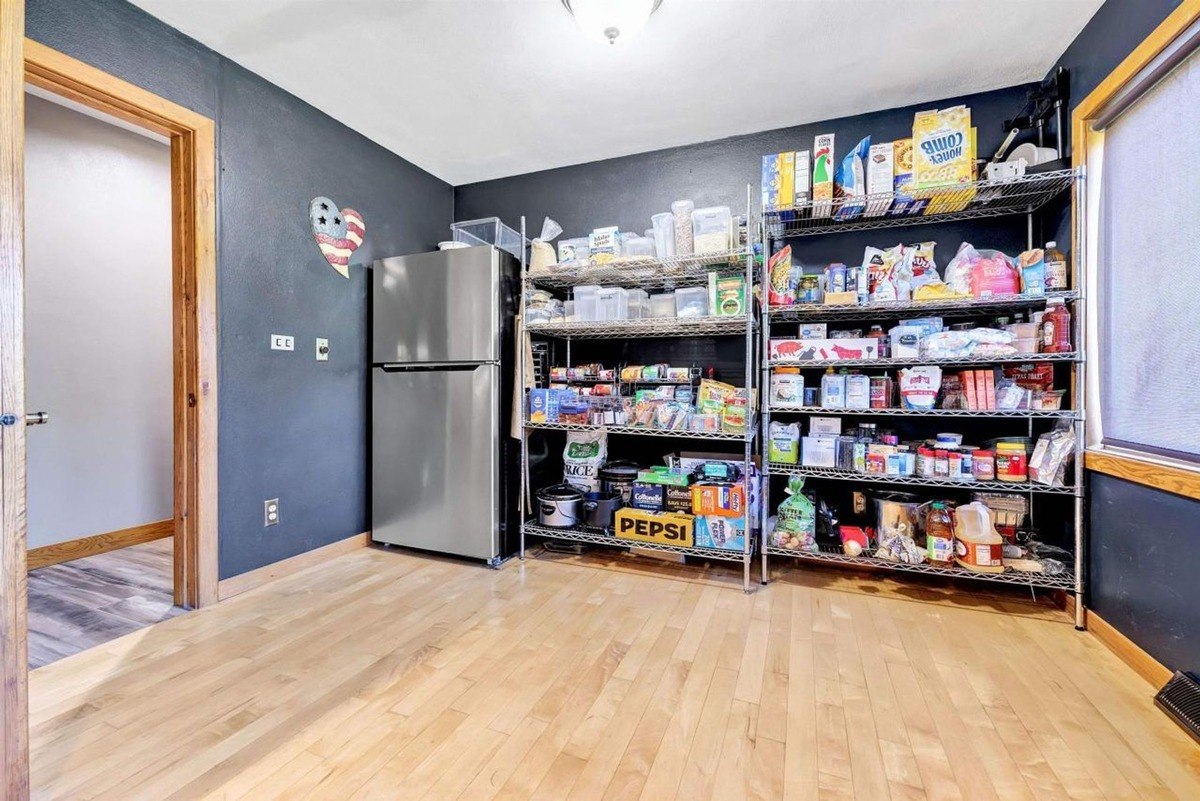 Pantry dark walls, wood floors, refrigerator, and wire shelving stocked with food.