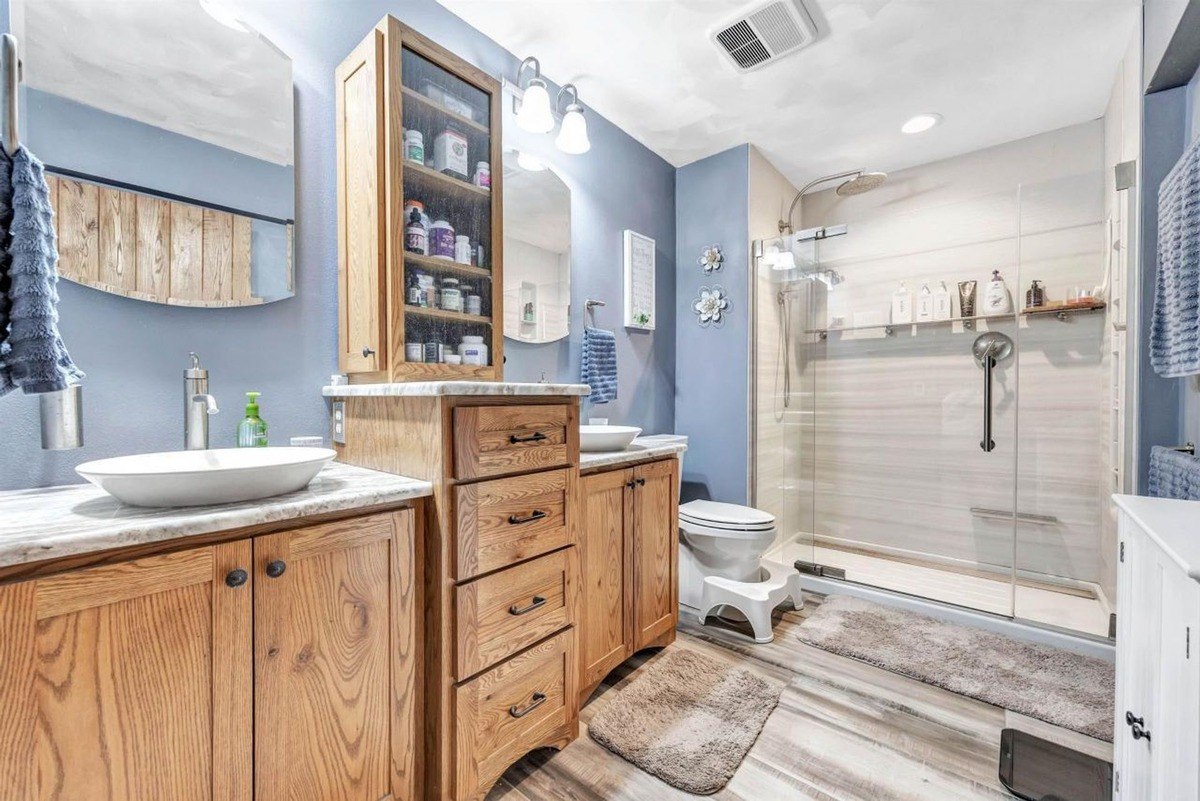 Bathroom has blue walls, wood cabinets, double sinks, and a walk-in shower.