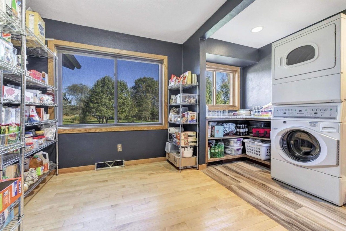 Room has dark walls, wood floors, wire shelving with food, and stacked washer and dryer.