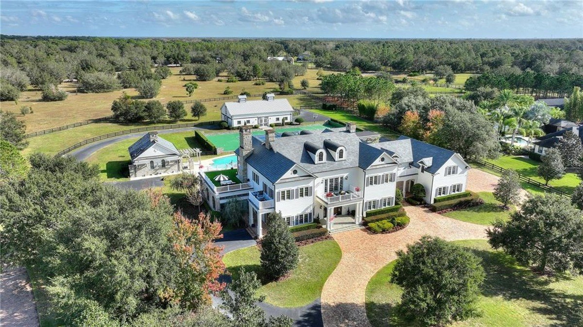 Large white house with a gray roof is situated on a sprawling property with a pool, barn, and other outbuildings.