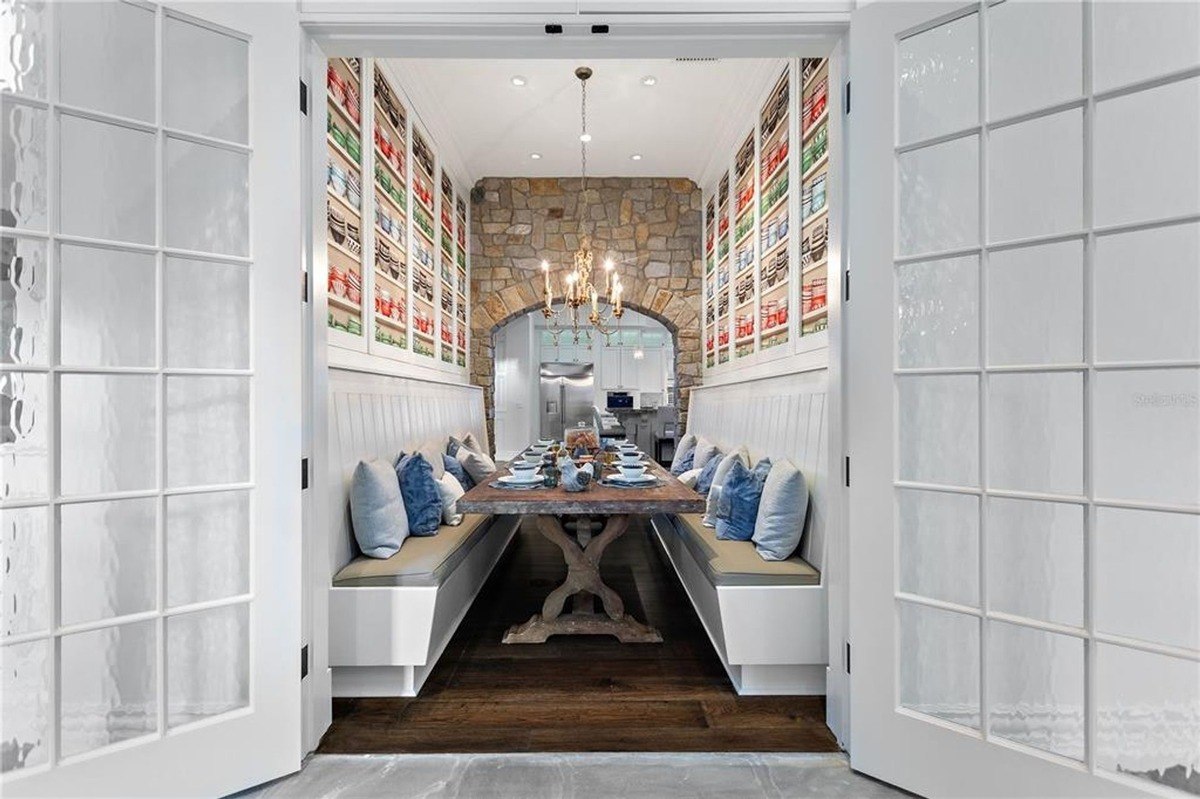 Breakfast nook has built-in seating, a long wooden table, and a stone wall, all viewed through open white doors with frosted glass panes.