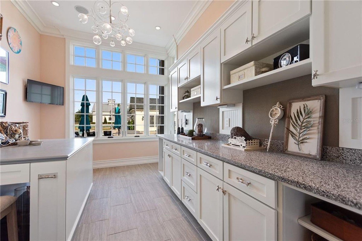 Bright room has white cabinets, granite countertops, and a large window overlooking a garden.