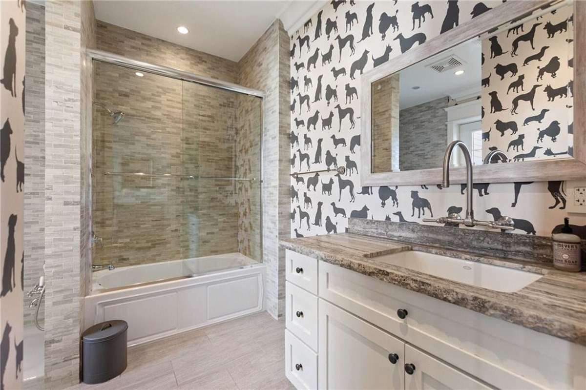 Bathroom features a bathtub, shower, and a vanity with granite countertop, all set against a wall with dog-themed wallpaper.