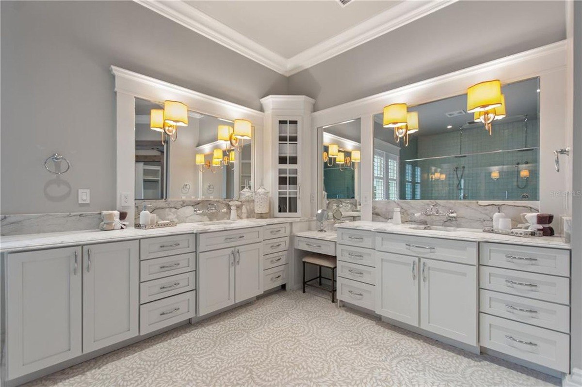 Large master bathroom features double vanities with granite countertops, gray cabinets, and patterned floor tiles.