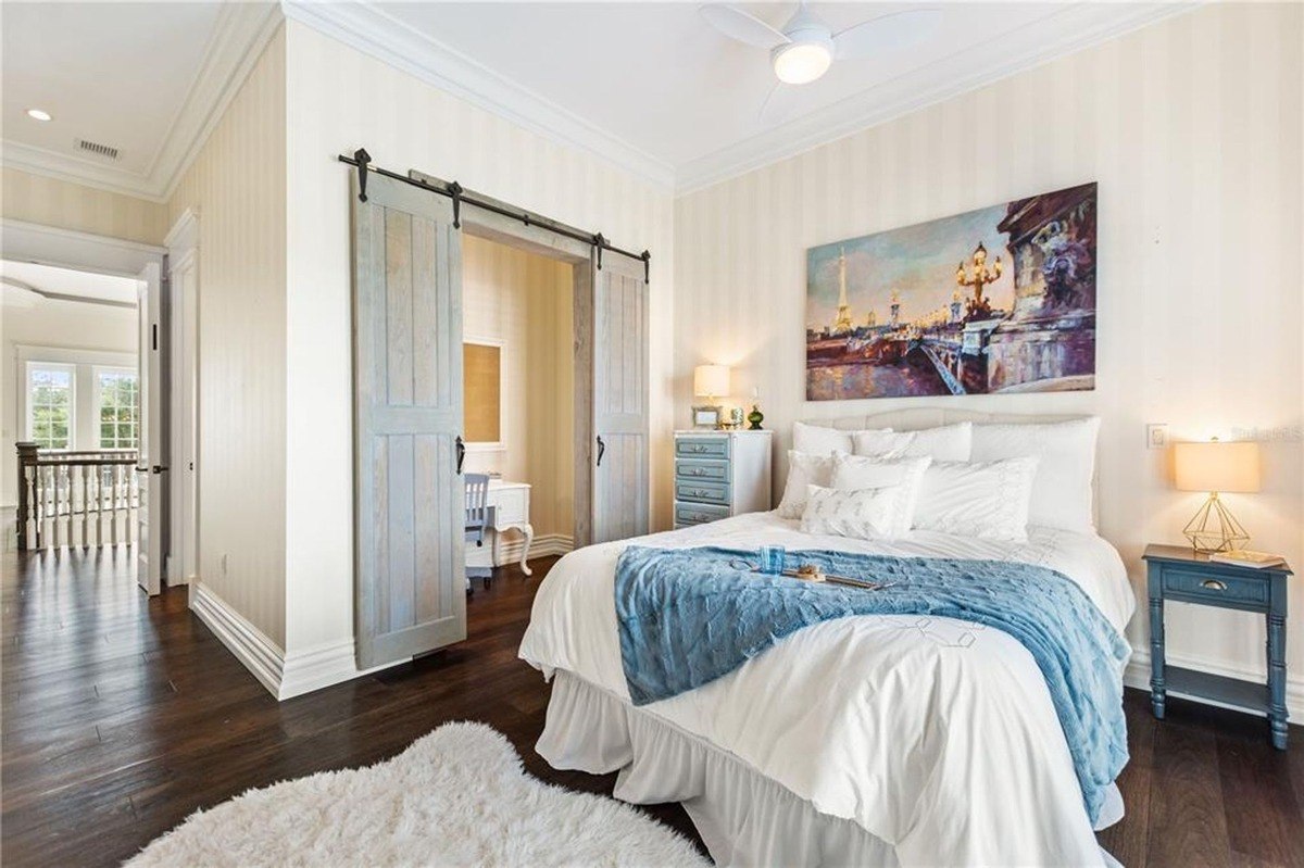 Bedroom features a bed with white bedding and a blue throw, dark hardwood floors, and a sliding barn door leading to an office.