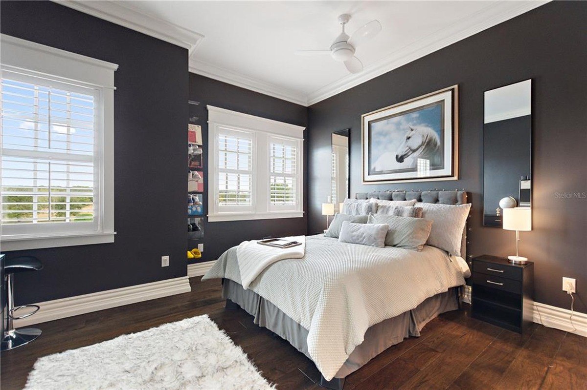 Bedroom features a bed with white bedding, dark walls, hardwood floors, and a ceiling fan.