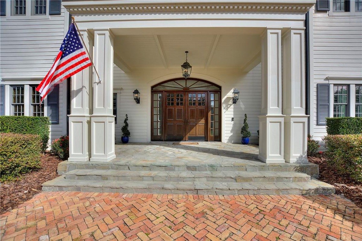 House entrance features a large wooden door, stone steps, and a brick walkway, with an American flag displayed on a porch post.