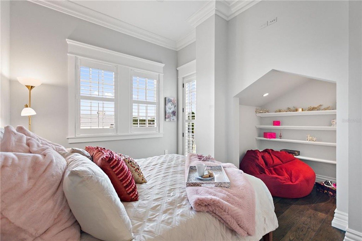 Bedroom features a bed with white bedding and pink throw, built-in shelves, and a red beanbag chair.