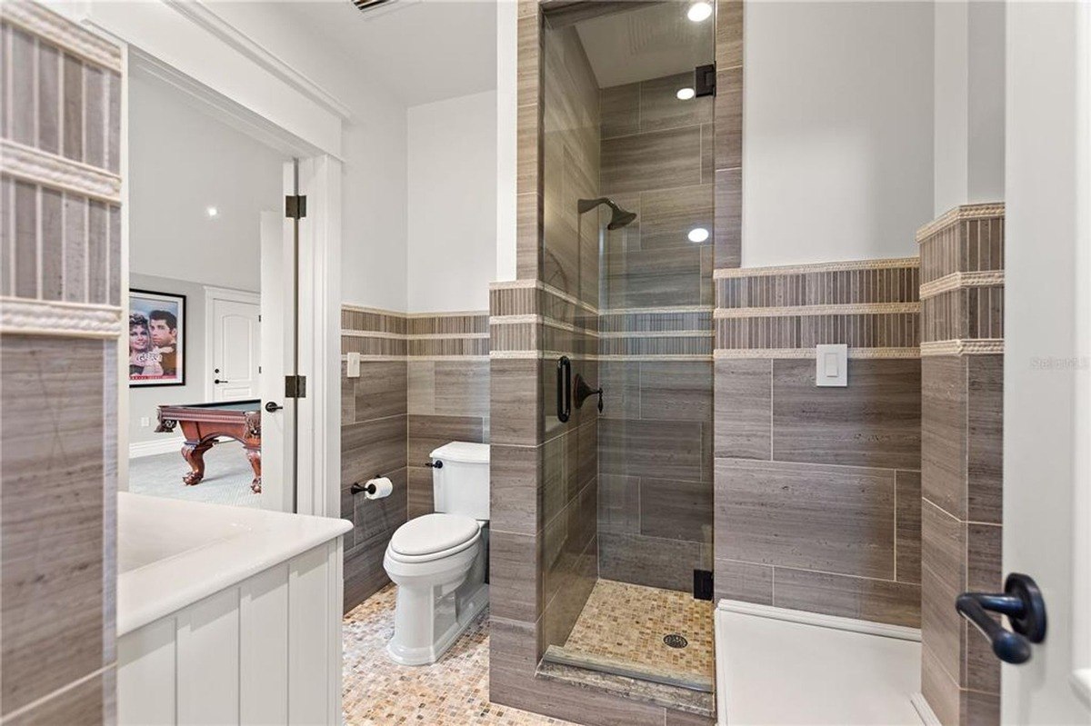 Bathroom features a toilet, shower with glass enclosure, and wood-look tile walls.