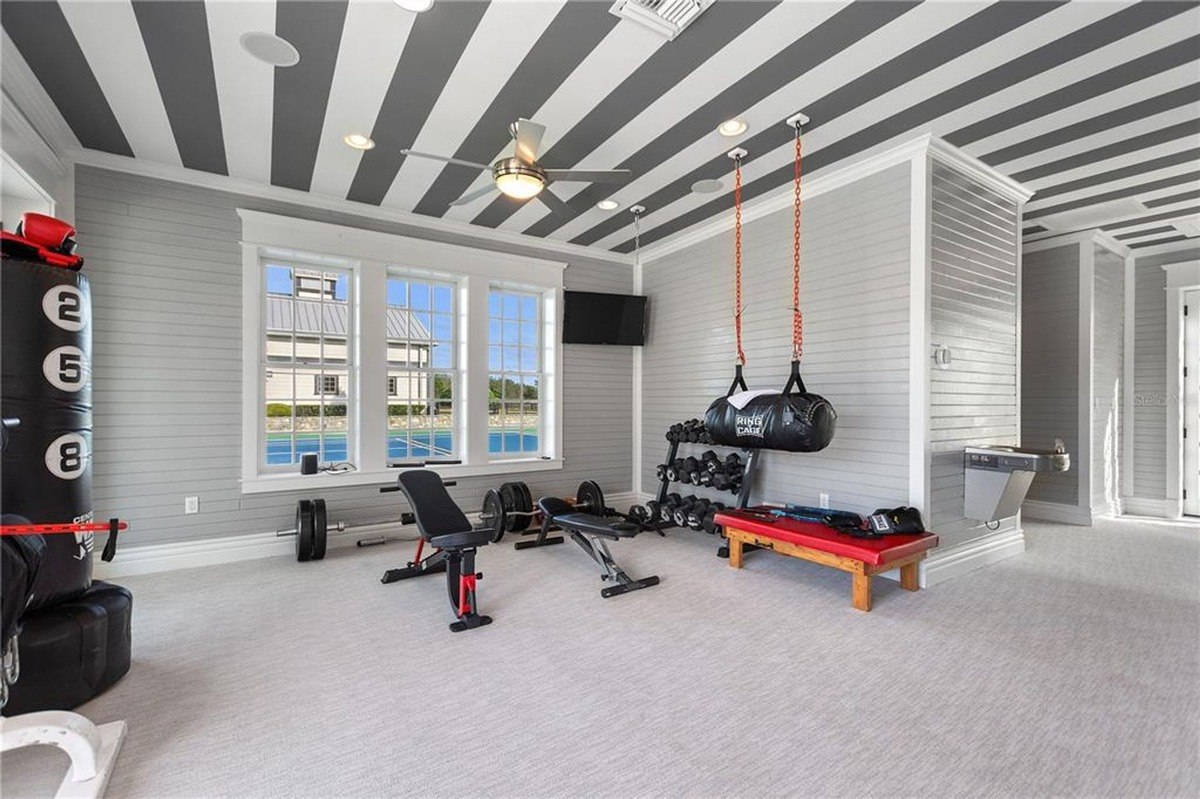 Home gym has weightlifting equipment, a punching bag, and a striped ceiling.