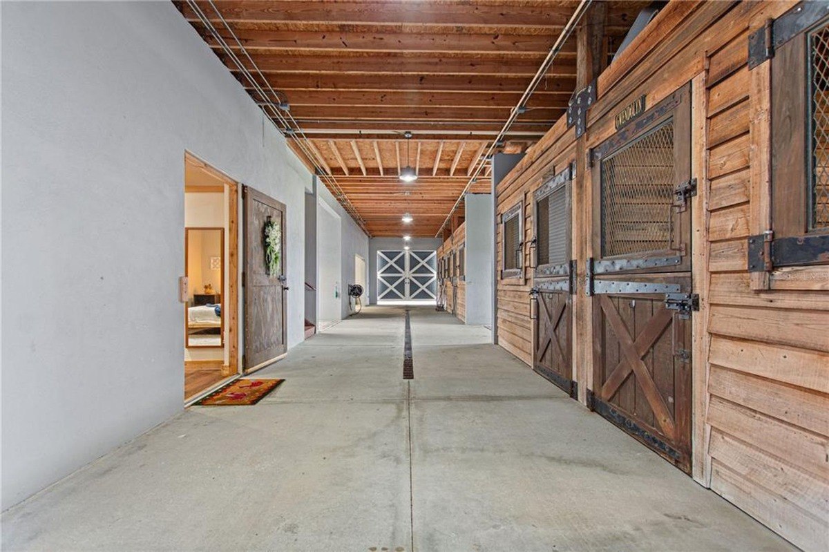 Long hallway has wooden stall doors on one side and a door to a bedroom on the other, leading to a large garage door at the end.