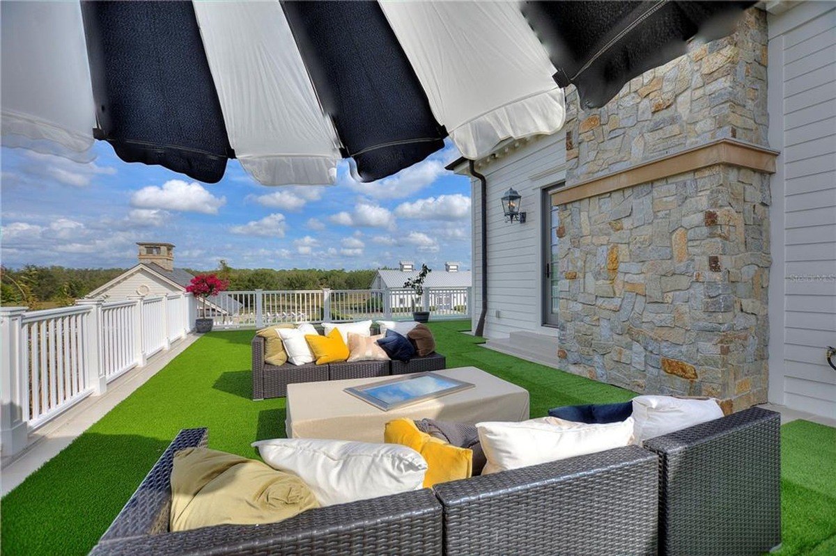 Rooftop patio features wicker furniture, artificial turf, and a stone fireplace, all under a black and white striped umbrella.