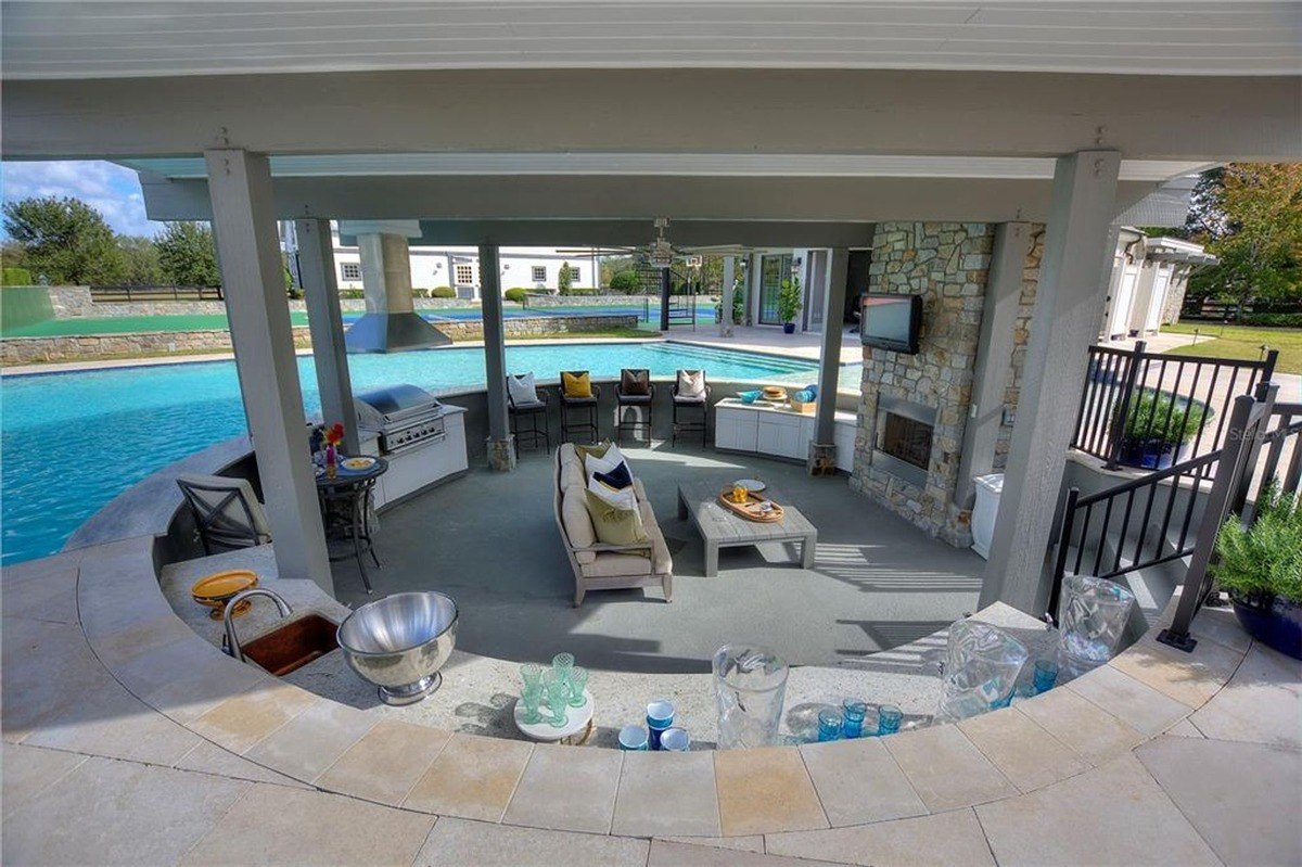 Outdoor kitchen and seating area overlooks a large pool, featuring a stone fireplace and built-in bar.