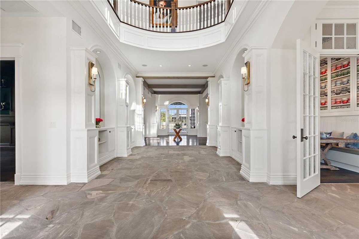 Elegant entryway features a two-story high ceiling with a curved staircase, white walls, and a stone floor.