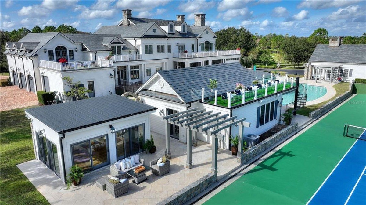 Aerial view shows a large white house with a pool, tennis court, and several outbuildings.