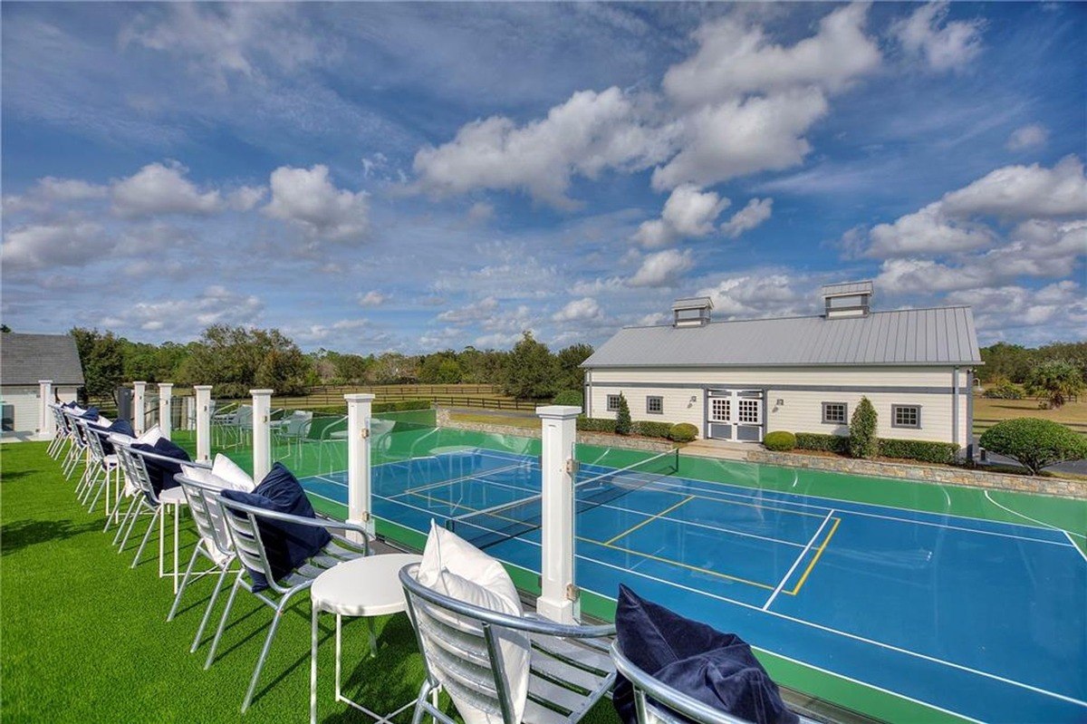 Outdoor patio with seating overlooks a blue tennis court and a large barn.