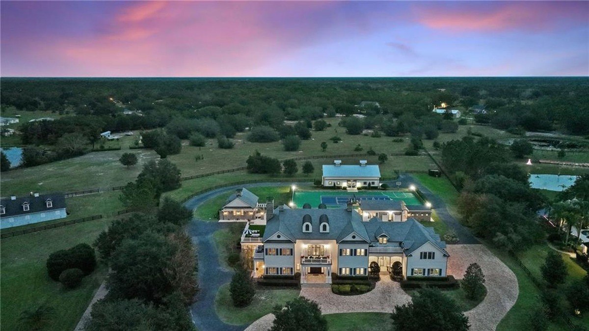 Large estate at sunset features a main house, outbuildings, and a tennis court.