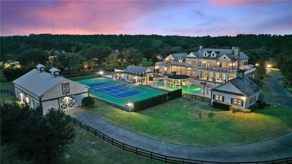 Aerial view of large estate at dusk shows main house, pool, tennis court, and barn.