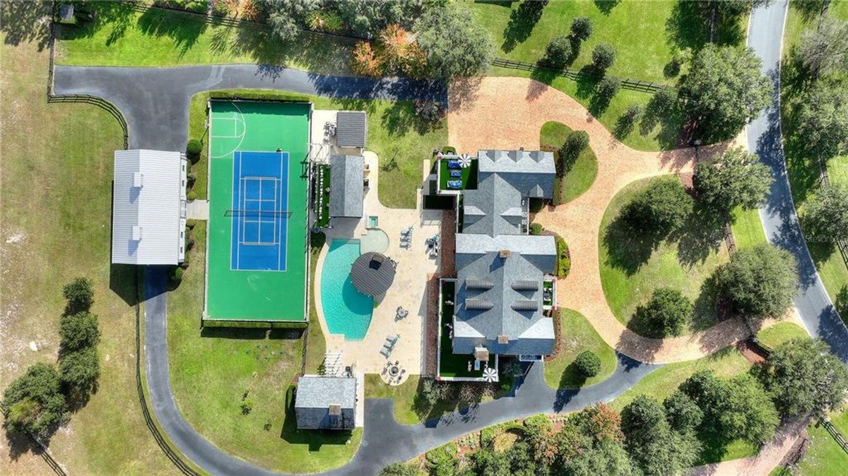 Aerial view shows a large house with a pool, tennis court, and barn on a sprawling property.