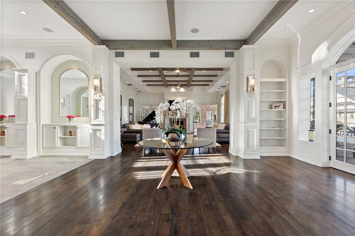 Spacious entryway has dark hardwood floors, white walls with built-in shelving, and a glass-top table with a large orchid arrangement.