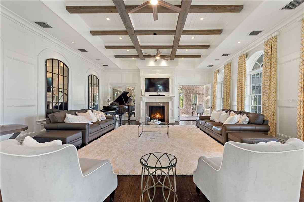 Large living room features a grand fireplace, two brown leather sofas, a large area rug, and exposed wooden beams on the ceiling.