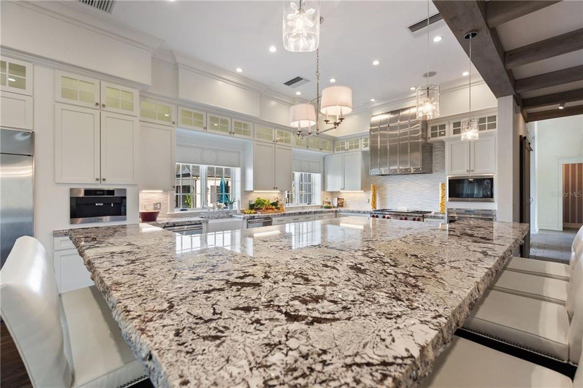 Large kitchen features a substantial granite countertop island, white cabinets, and stainless steel appliances.