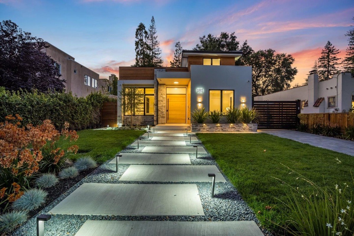 Modern exterior at dusk a contemporary home with a well-lit walkway and lush landscaping at sunset.