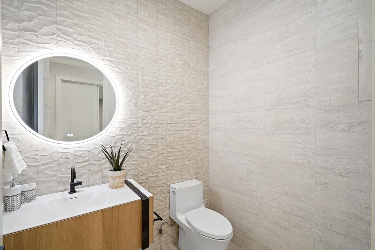 Powder room with textured wall a modern powder room with an illuminated oval mirror, a floating vanity, and a textured accent wall.