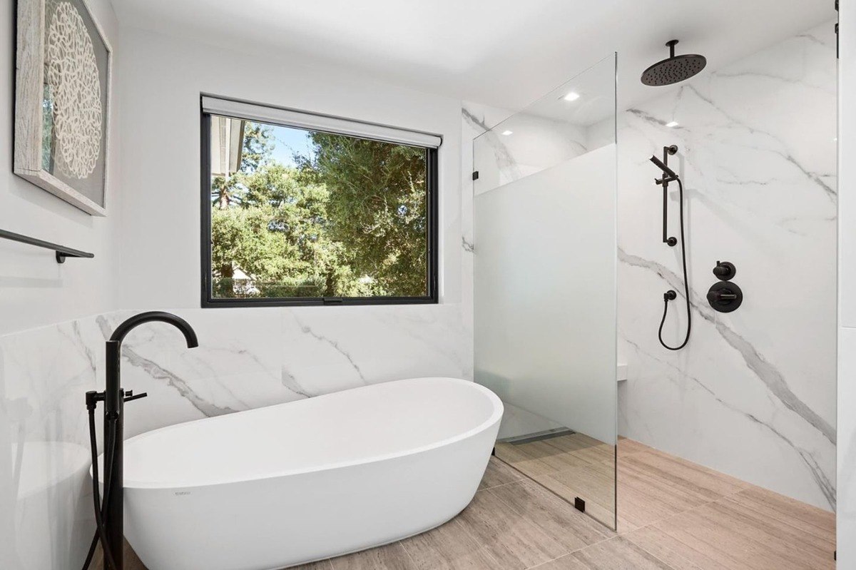 Spa-like bathroom with nature view a bathroom with a large window, freestanding tub, and marble-accented shower.