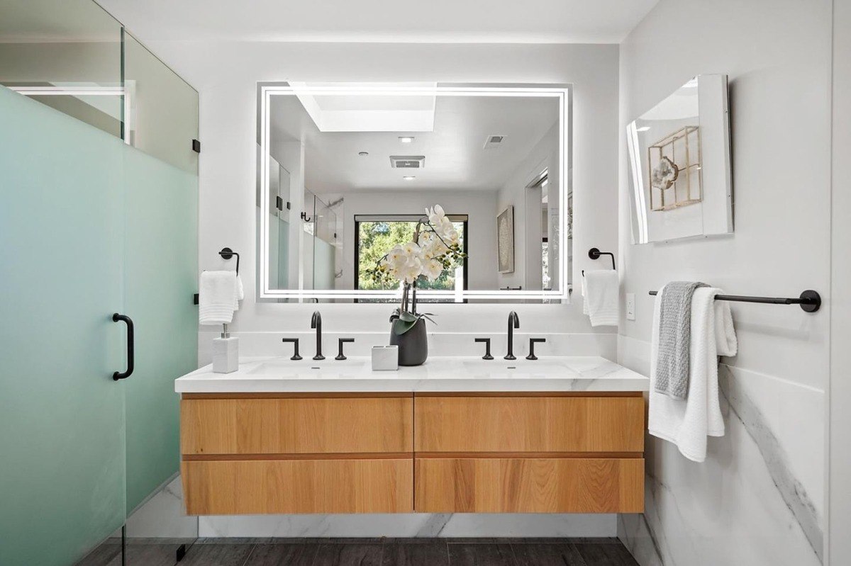 Double vanity with led mirror a dual-sink vanity with wood cabinets, an led-lit mirror, and matte black fixtures.