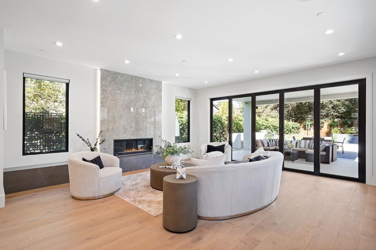 Open concept family room family room with a fireplace, large glass doors leading to an outdoor seating area, and modern decor.