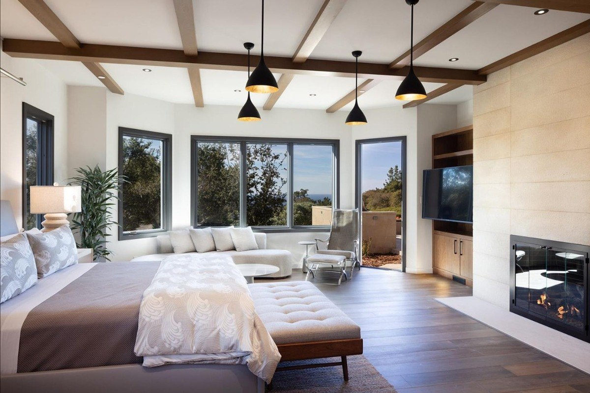 Luxurious bedroom with a plush bed, a fireplace, and large windows offering breathtaking views of the surrounding landscape.