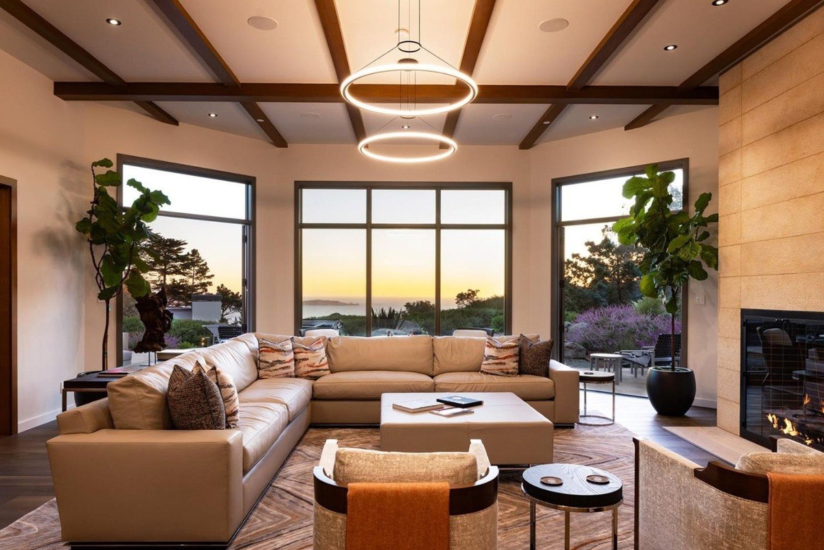 Cozy living room with a large sectional sofa, a fireplace, and expansive windows offering breathtaking views of the sunset over the ocean.