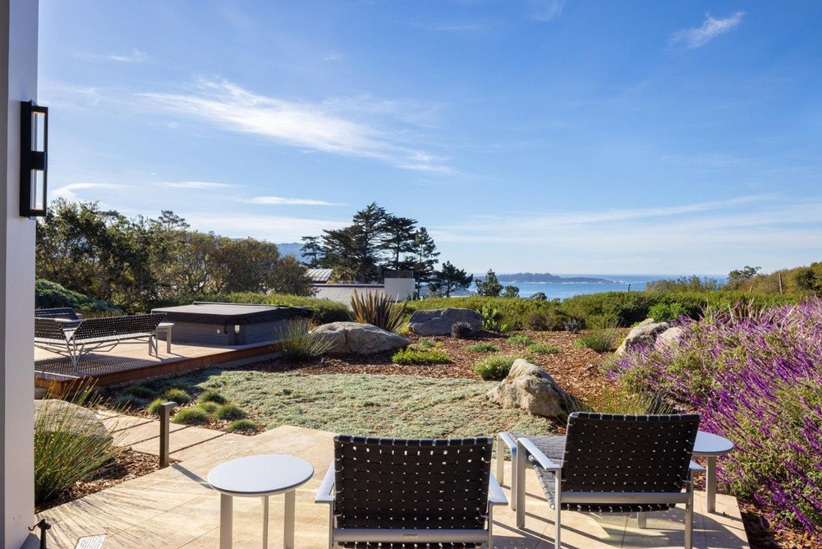 Patio with seating overlooking a beautifully landscaped yard with a hot tub, offering stunning views of the ocean and surrounding landscape.