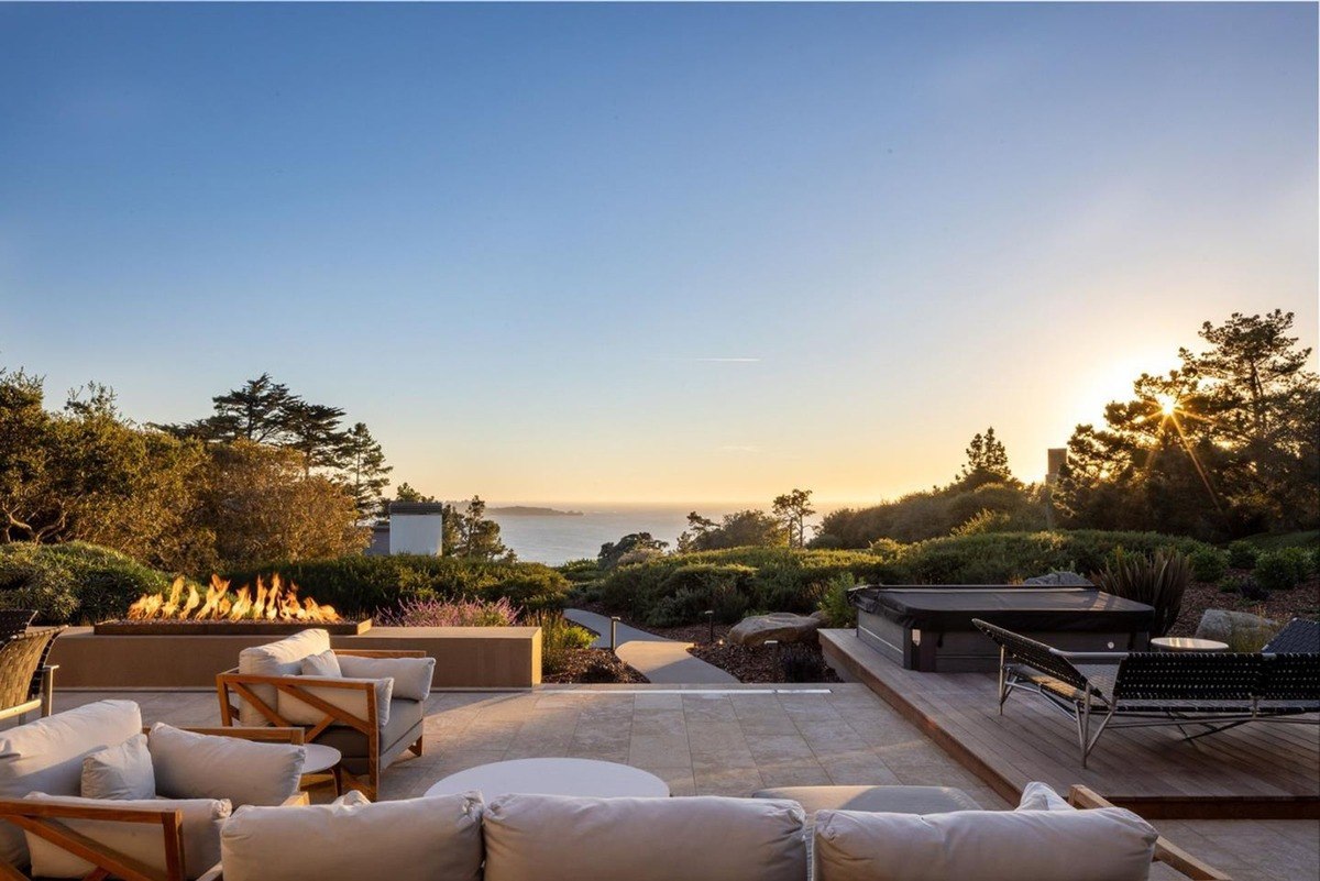 Stunning outdoor living space with a fire pit, a hot tub, and comfortable seating, all overlooking a breathtaking sunset over the ocean.