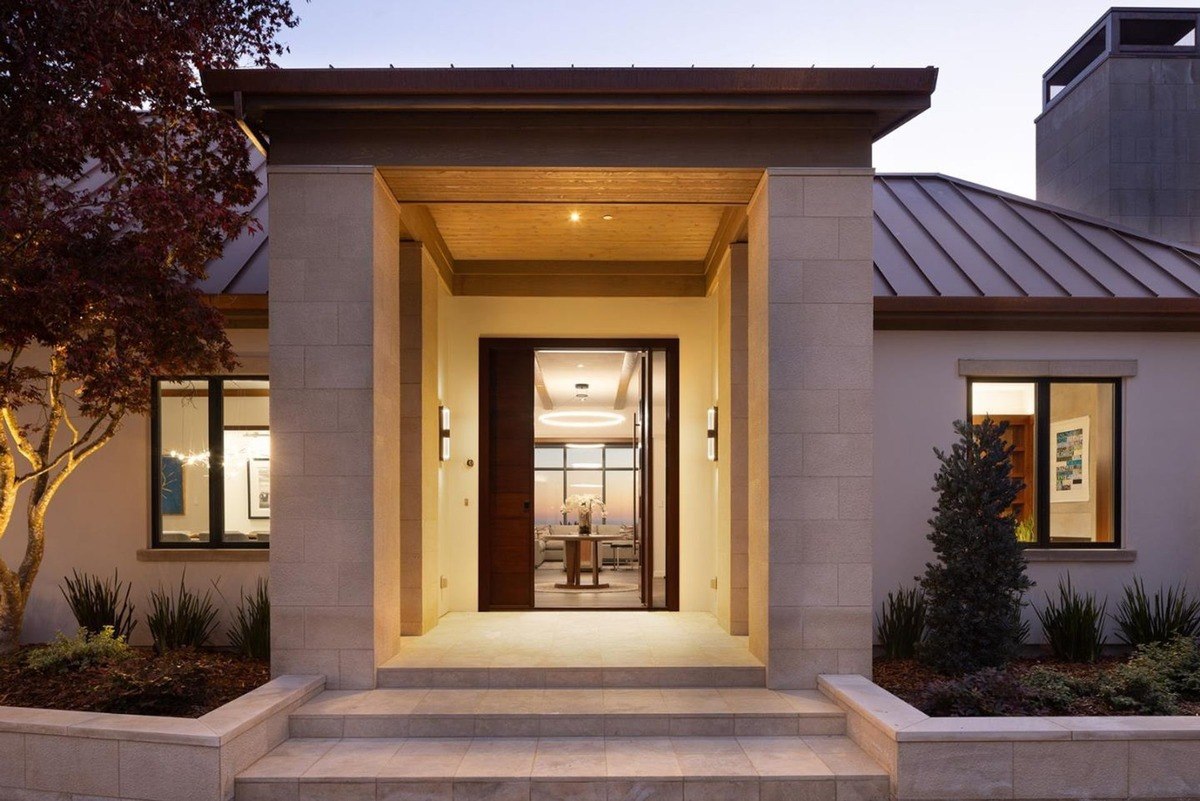 Entrance of the house with a double-door entryway, flanked by stone pillars and illuminated by warm lighting.