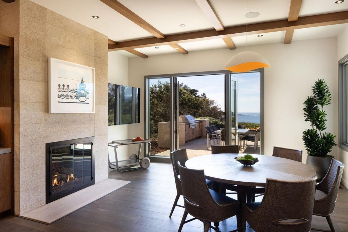 Cozy dining nook with a fireplace, a round table, and chairs, offering access to a patio with stunning ocean views.