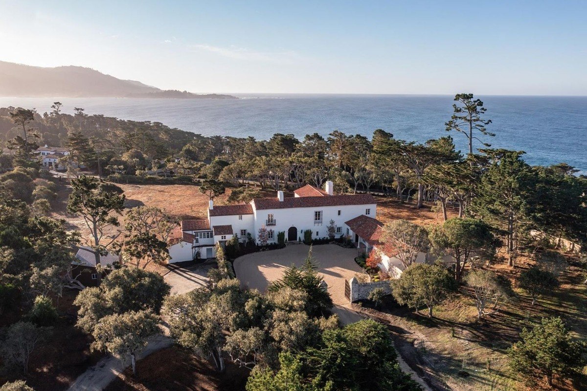 Expansive coastal view showcases a magnificent house nestled among trees, blending nature and architecture beautifully.