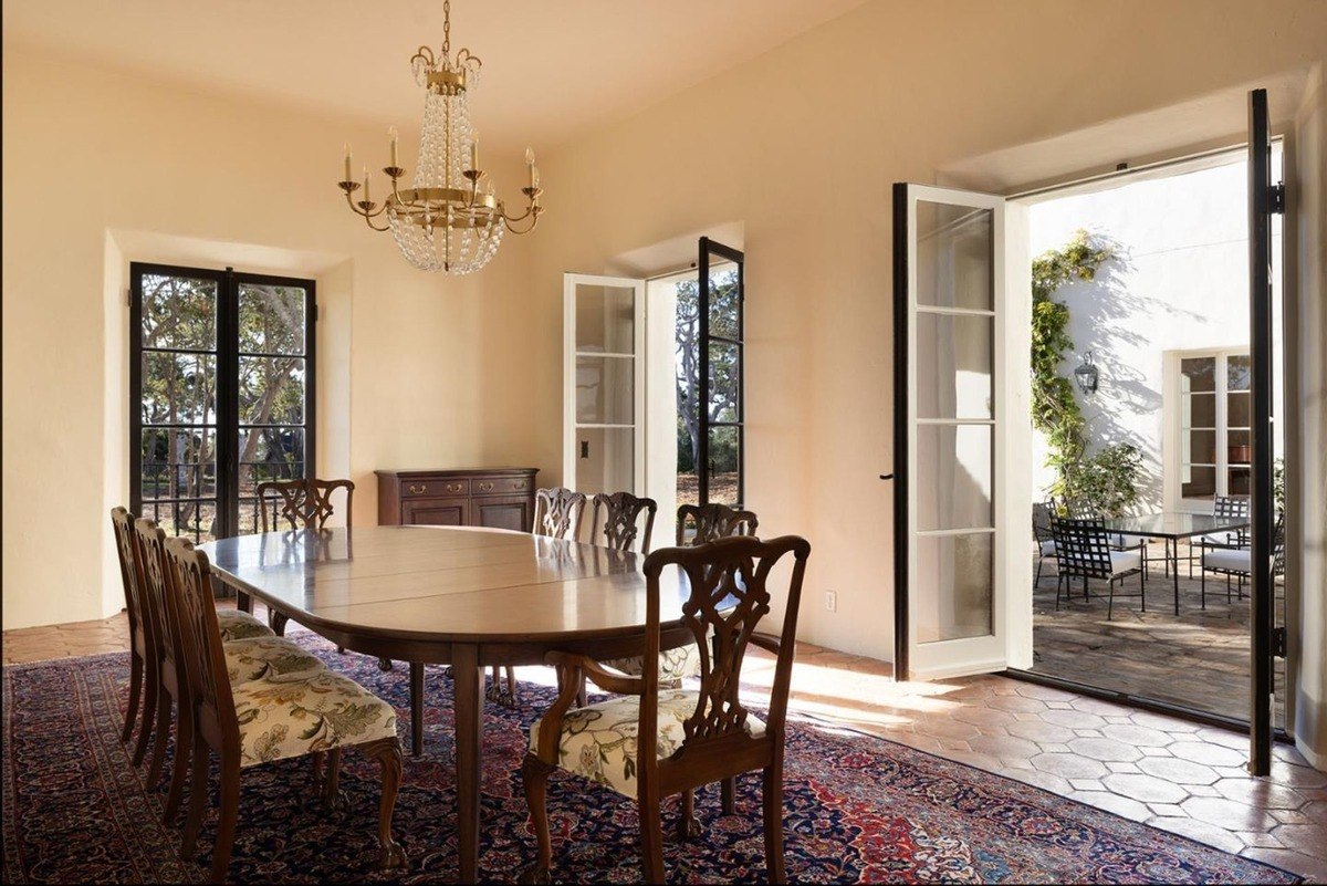 Formal dining room with a large table, elegant chairs, and a chandelier, offering access to an outdoor patio through French doors.