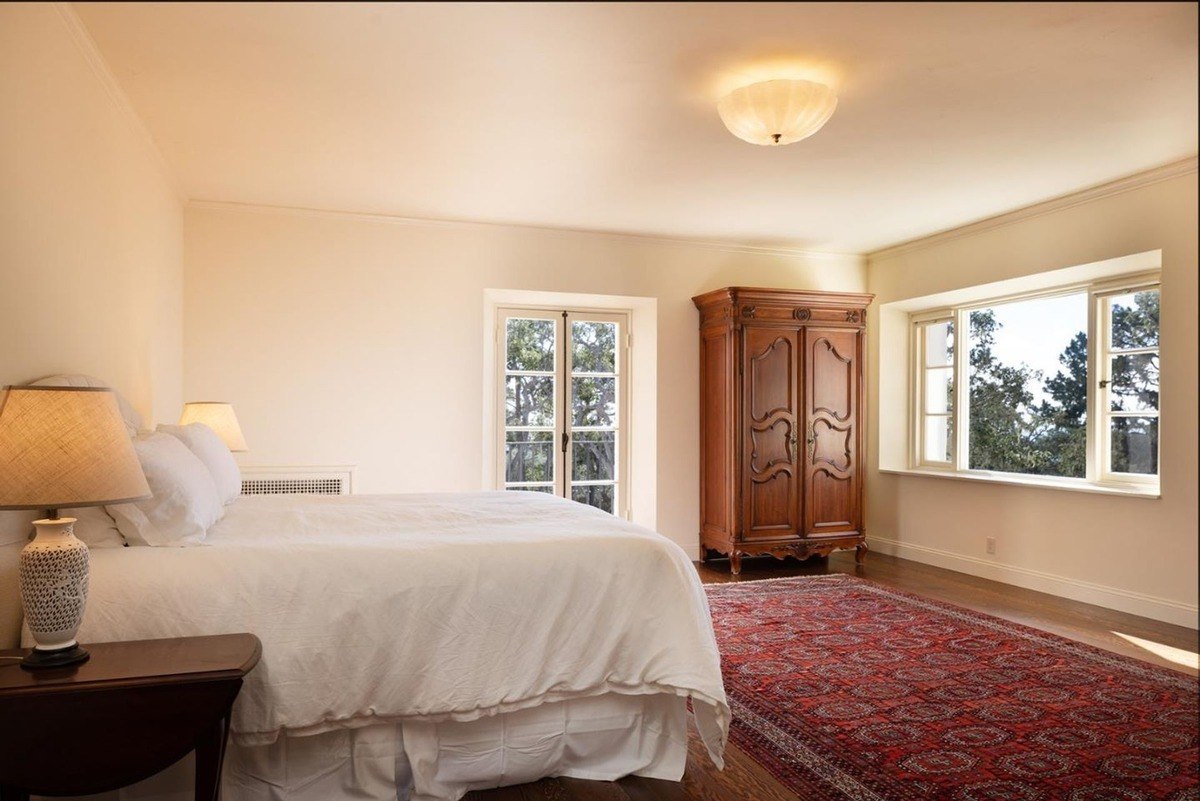 spacious bedroom with a king-sized bed, a vintage armoire, and large windows offering breathtaking views of the surrounding landscape.